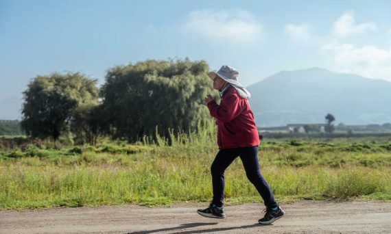 A woman in sportswear jogs along a rural road, surrounded by lush countryside and mountains.